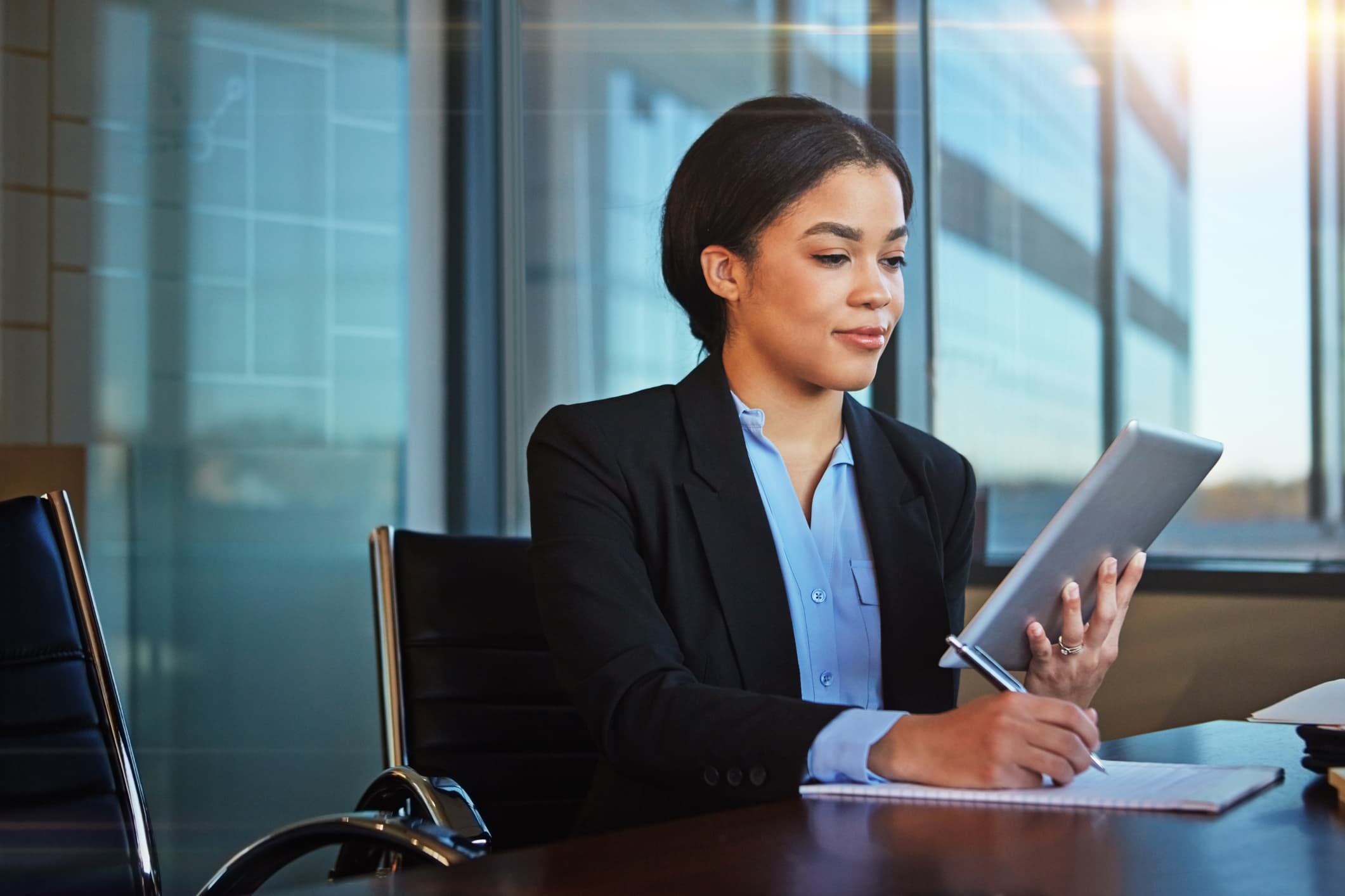 Woman sitting at a desk holding a tablet and writing down notes