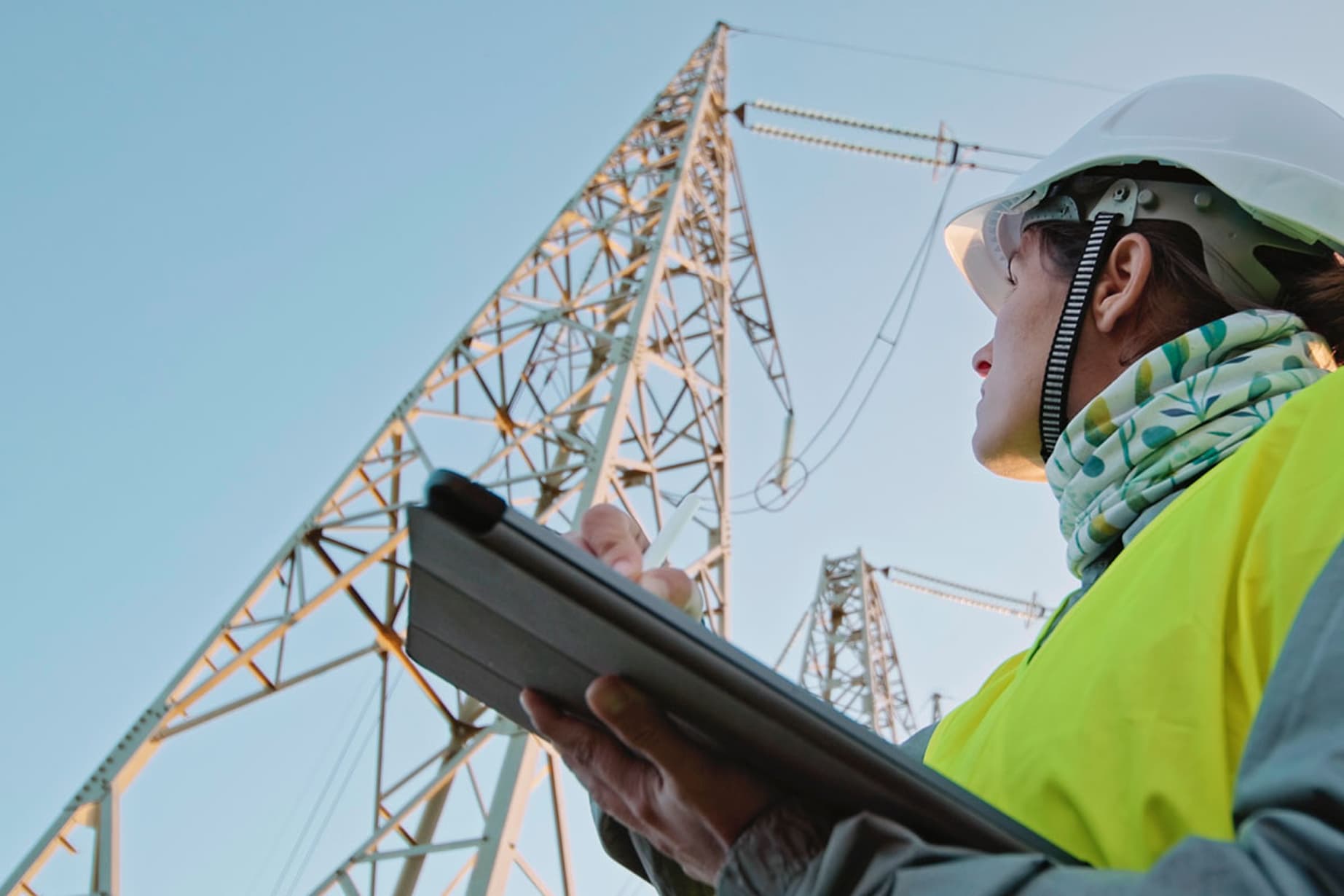Woman with a hard hat holding a tablet looking at an electric pole
